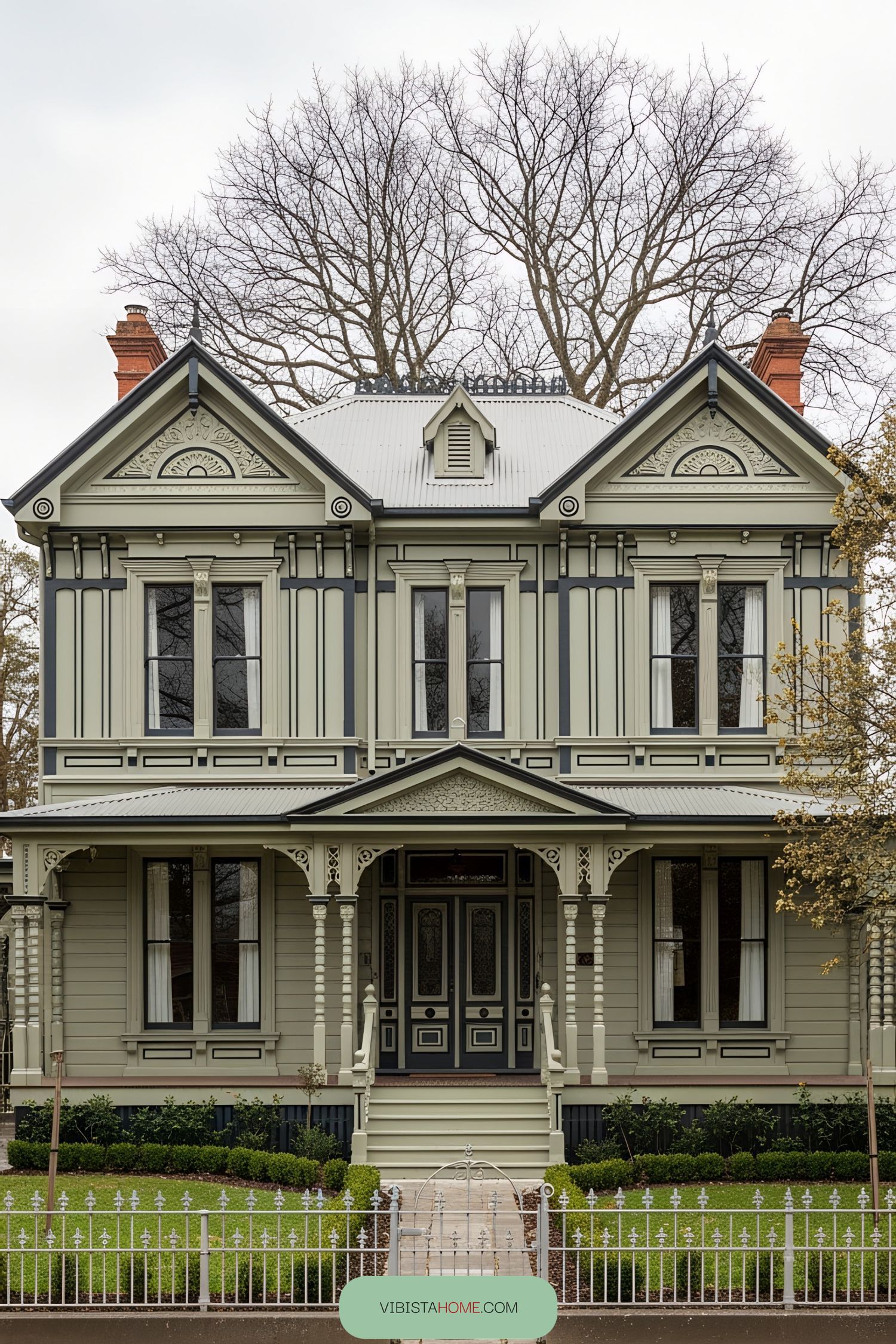 Victorian style house with elaborately detailed architecture, flanked by bare trees
