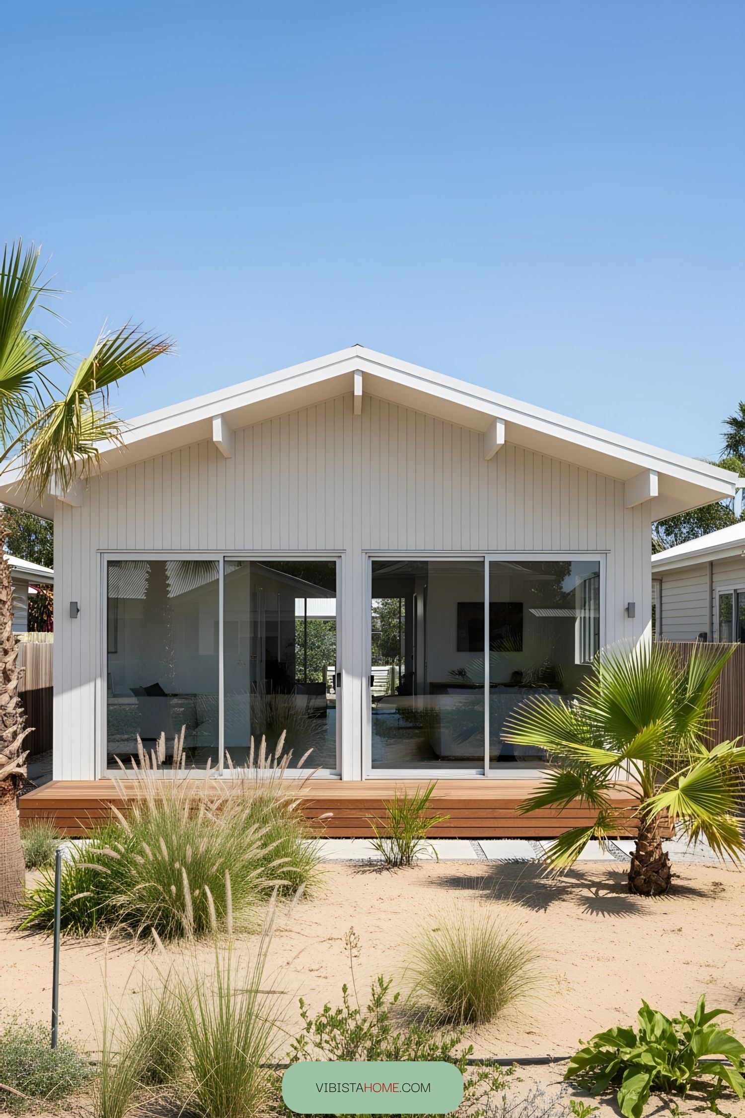 White bungalow with sliding glass doors and a sandy garden