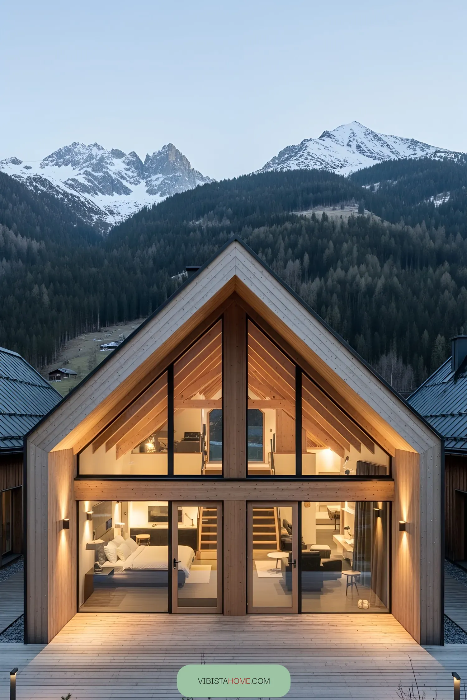 Modern wooden lodge with floor-to-ceiling windows set against a snowy mountain backdrop