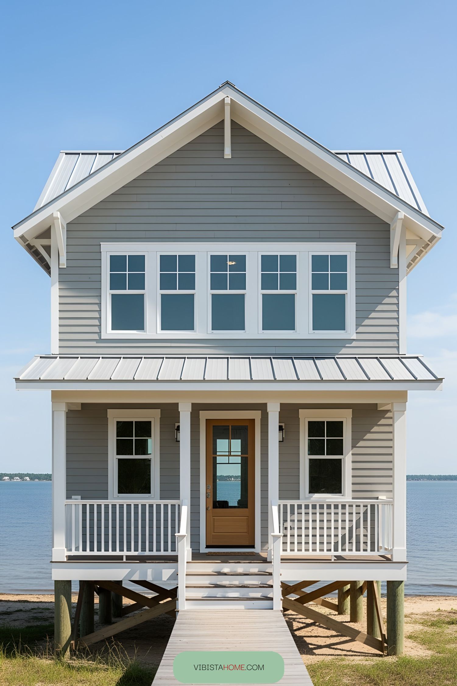 Elevated beach house with gray siding and white trim overlooking calm waters