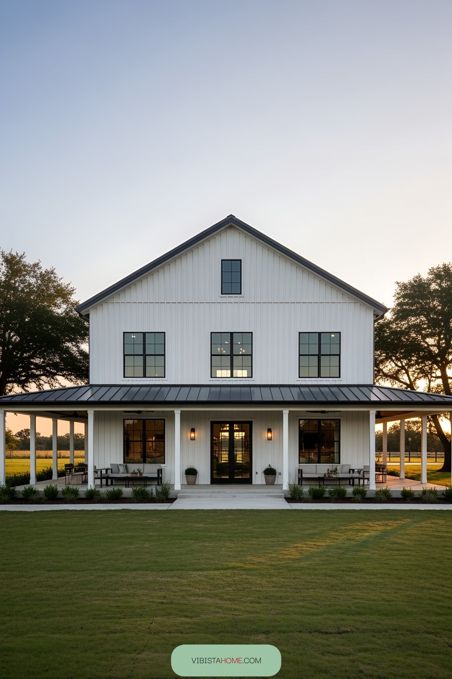 White barnhouse with a wraparound porch and sunset view