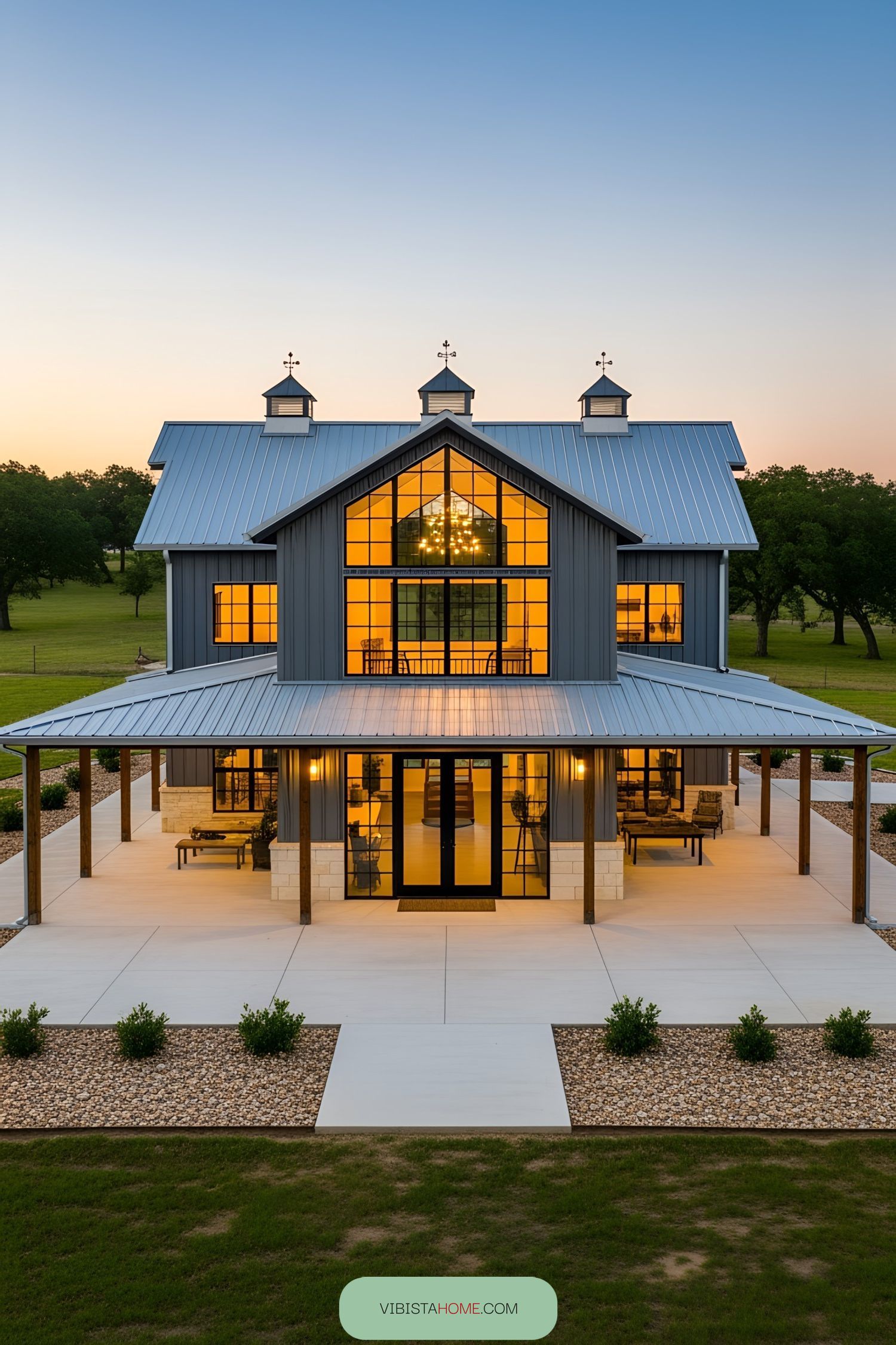 A modern barndominium with a wraparound porch at sunset